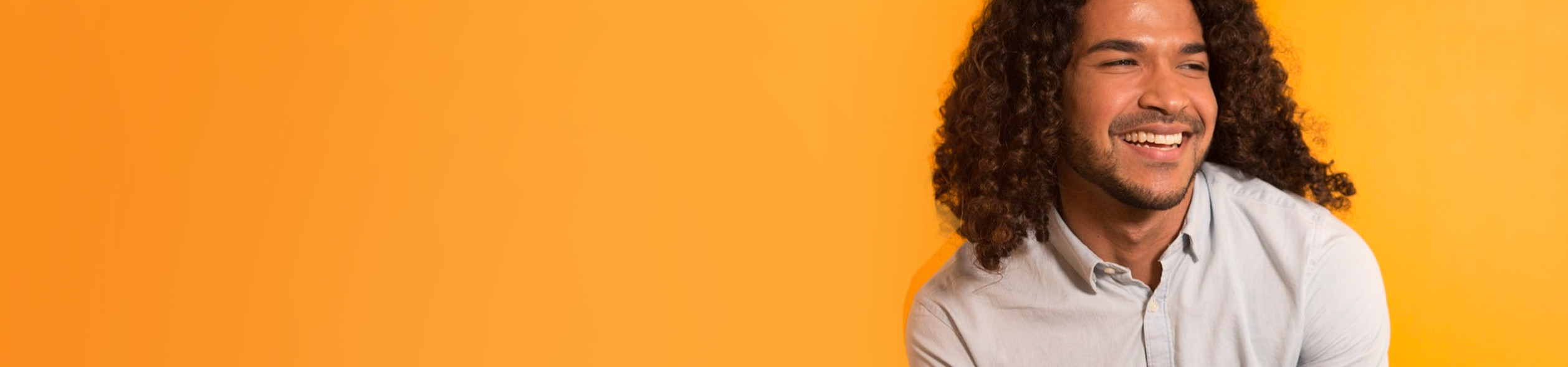 Persona de cabello rizado, sonriendo, contra un fondo naranja