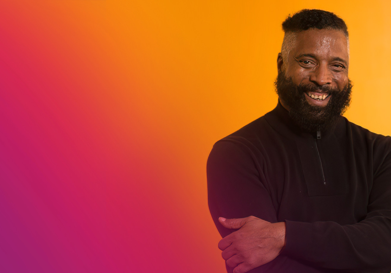 Smiling man in front of orange-red background.
