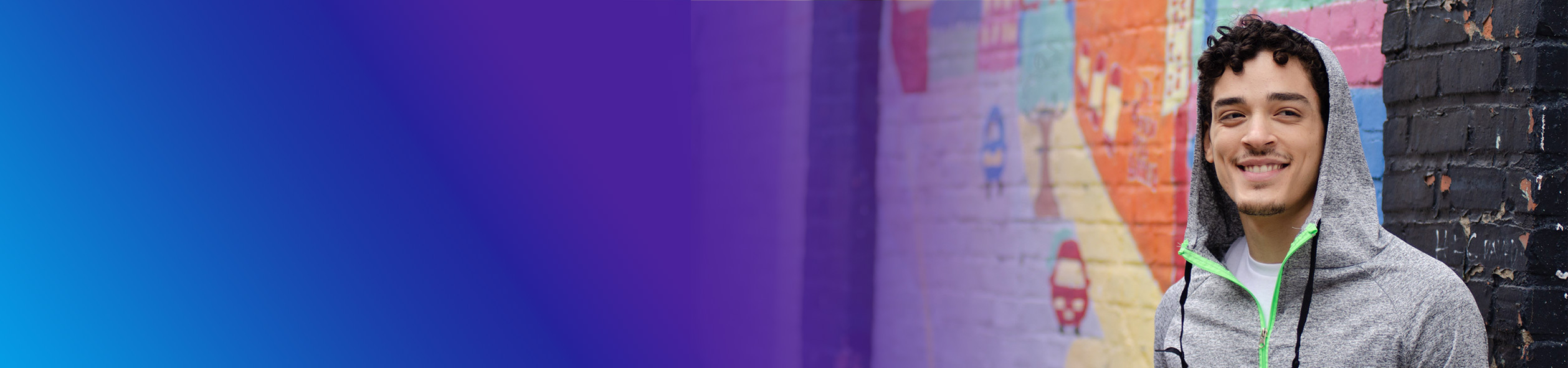 Person wearing hoodie in front of colorful wall mural
