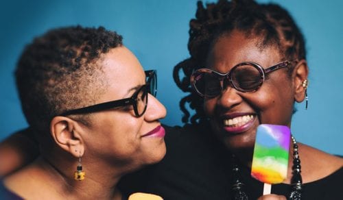 Two women holding rainbow popsicles.