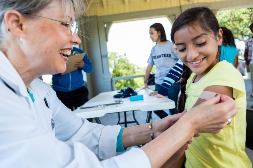 Cheerful doctor places adhesive bandage on preteen girl’s arm